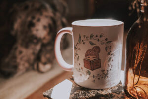 Magical mug from the Alex+A collection. Girl with pink hair, reading a book. Floral wreath around her.