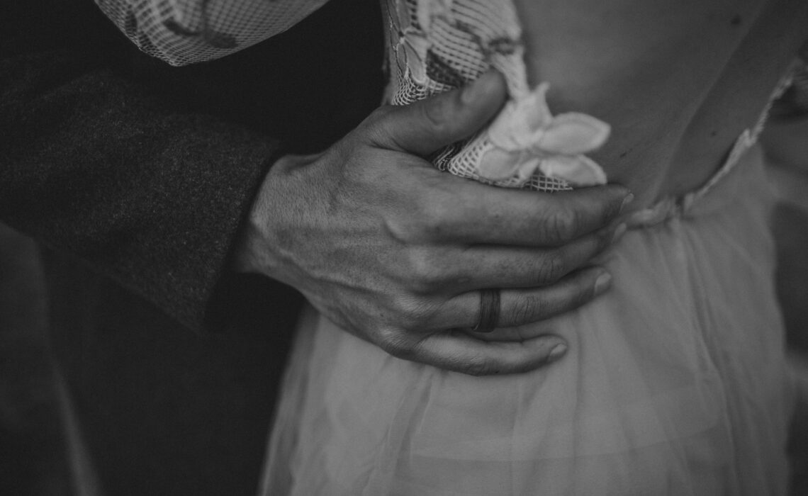Close-up wedding photo of a groom's hand on the bride's waist.