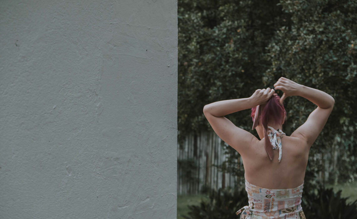 A girl seen walking away from the camera. She is tying her pink hair.