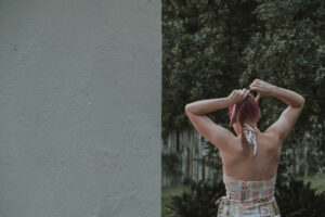 A girl seen walking away from the camera. She is tying her pink hair.